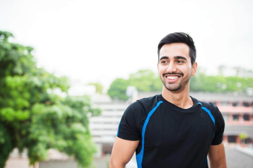 A man smiling confidently and looking energetic, perhaps stretching or preparing for a workout, bright natural light, realistic photo